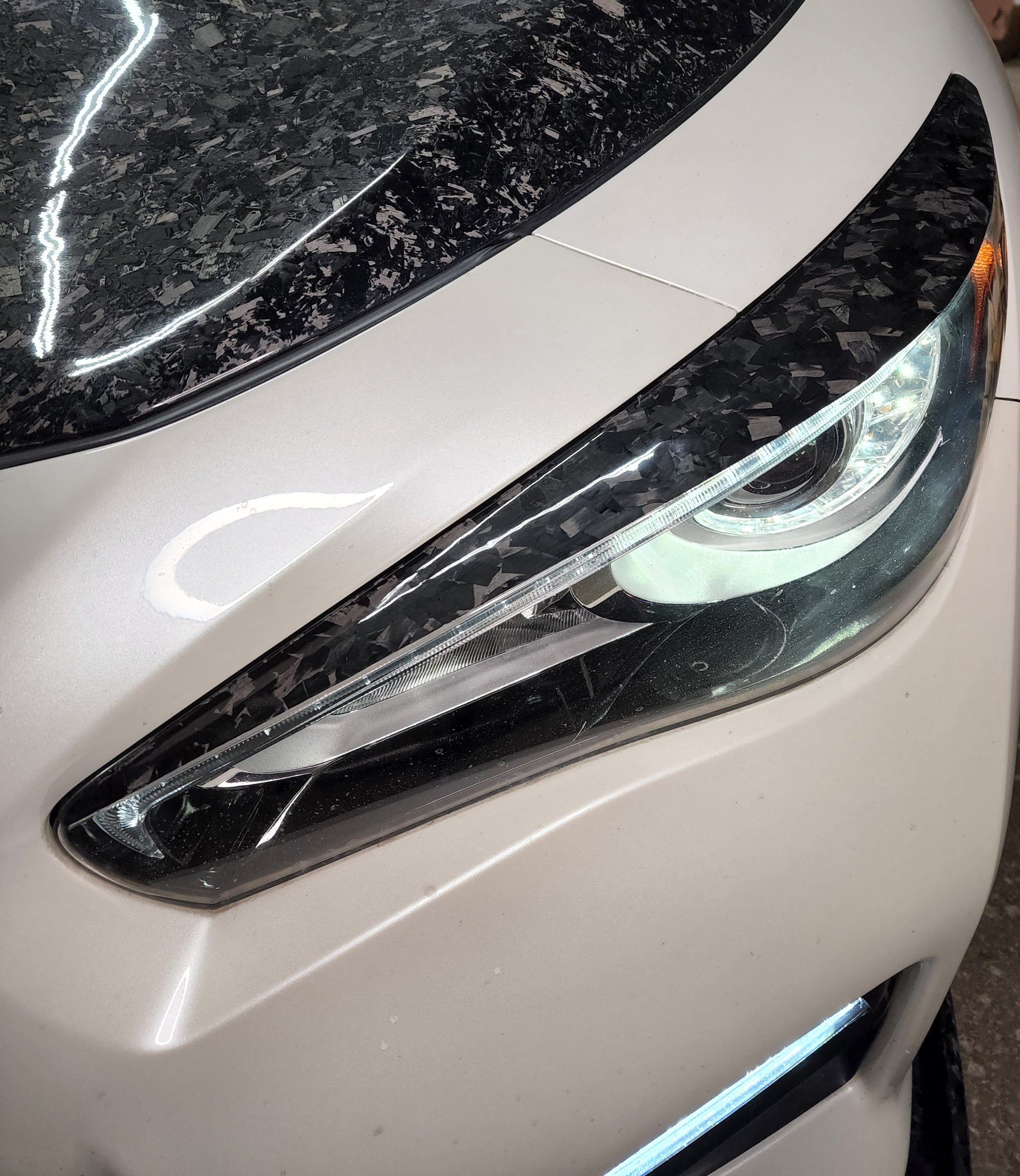 Close-up of Carbon Fiber Headlight Eyelid for Infiniti Q50 2014-2023, showcasing the high-quality material and texture.