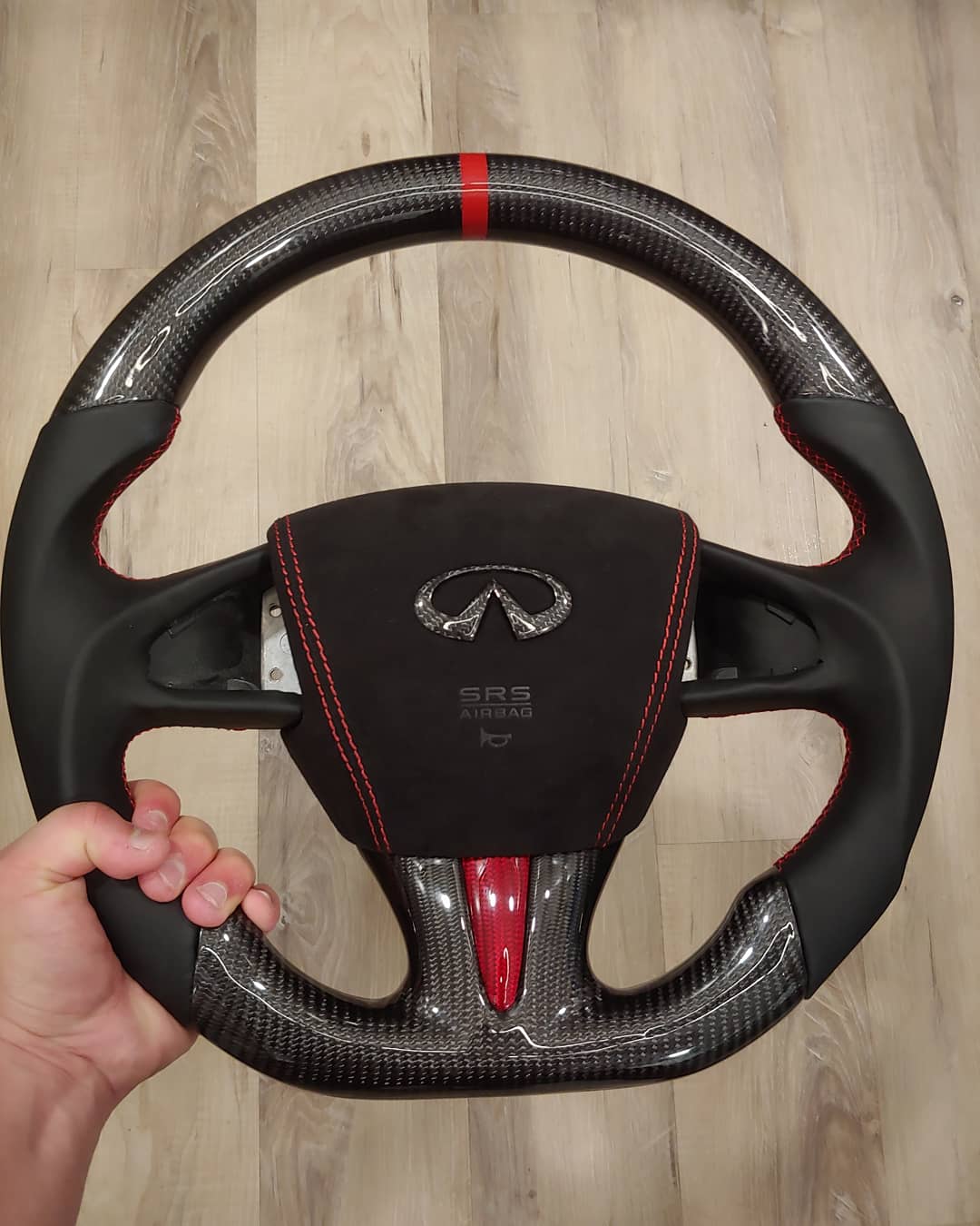 Traditional CarbonFiber Steering Wheel design with standard thumb holders, a red accent, red stitching, and a central red stripe for Infiniti Q50 2014-2017.